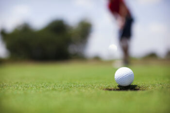 Man putting golf ball in the hole on a putting green 5616x3744